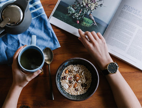 Person reading magazine while drinking coffee eating breakfast